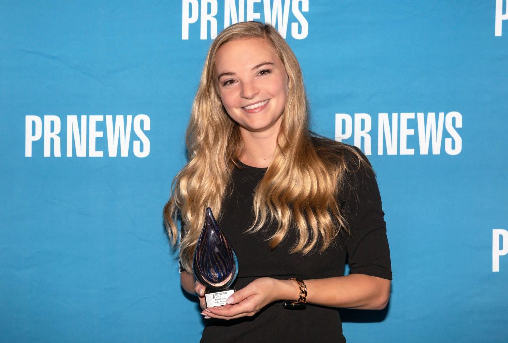 Blue PRNEWS background with young blonde woman (Taylor) holding an award.
